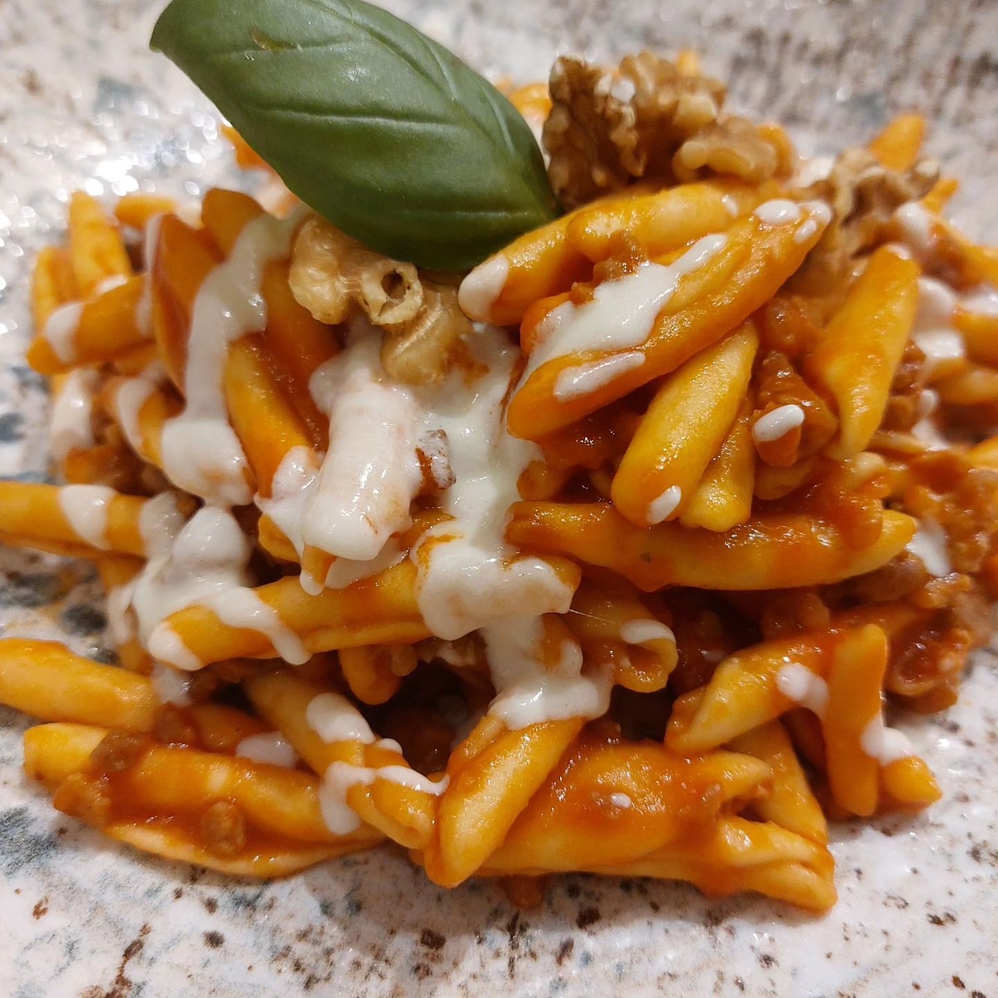 Pasta al sugo di pomodoro e formaggio fuso, guarnita con una foglia di basilico su un piatto maculato.