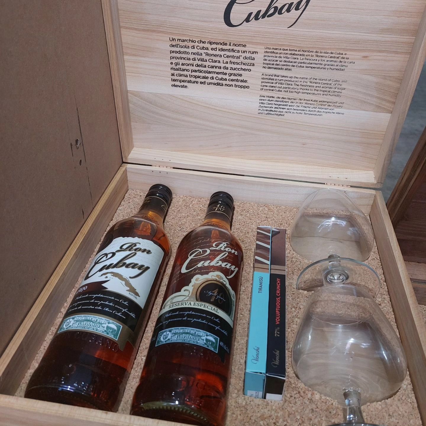 Confezione regalo in legno con due bottiglie di rum, un piccolo biglietto di auguri e un calice.