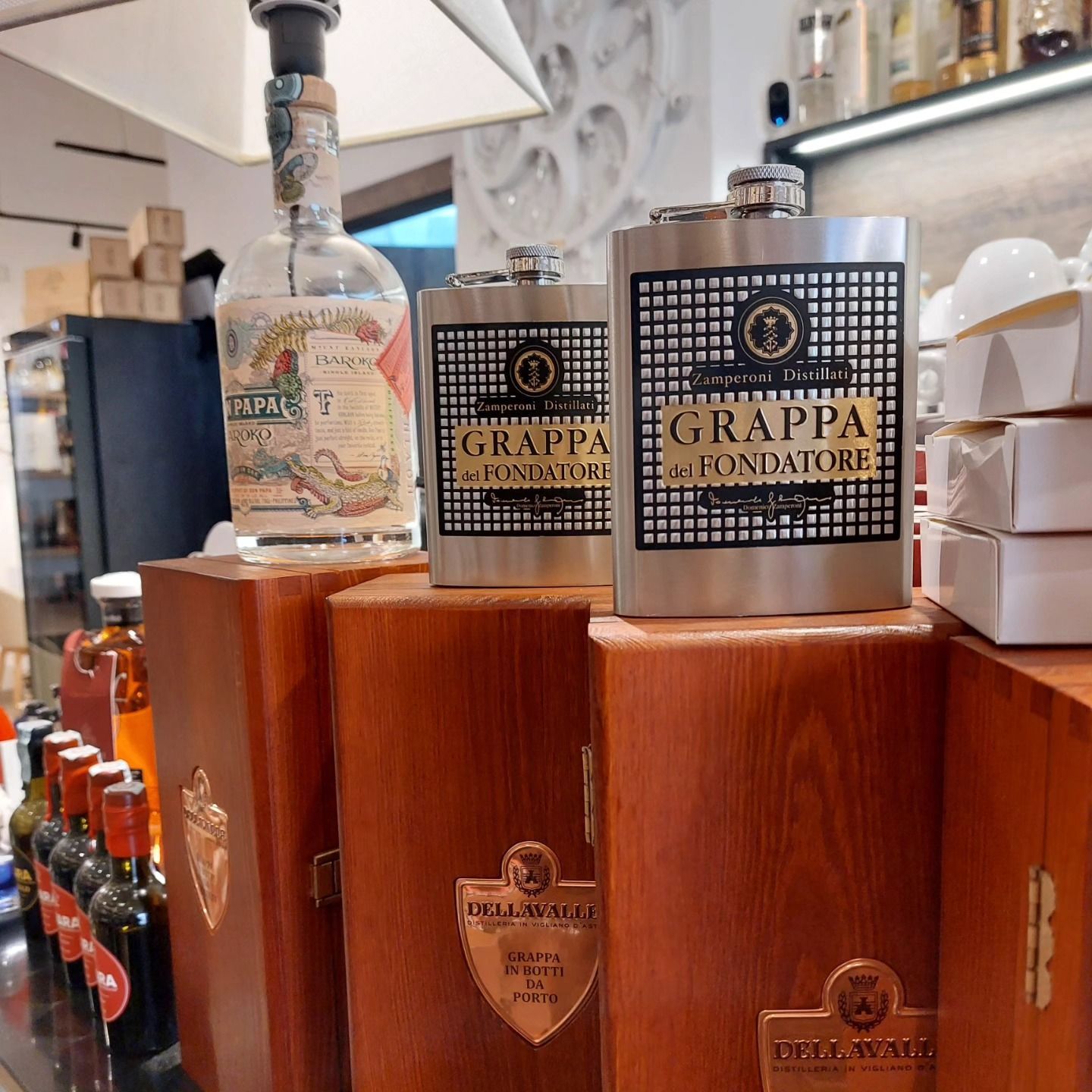 In un negozio, tre bottiglie di grappa sono esposte su un supporto di legno, di cui due con l'etichetta Grappa Fondatore.