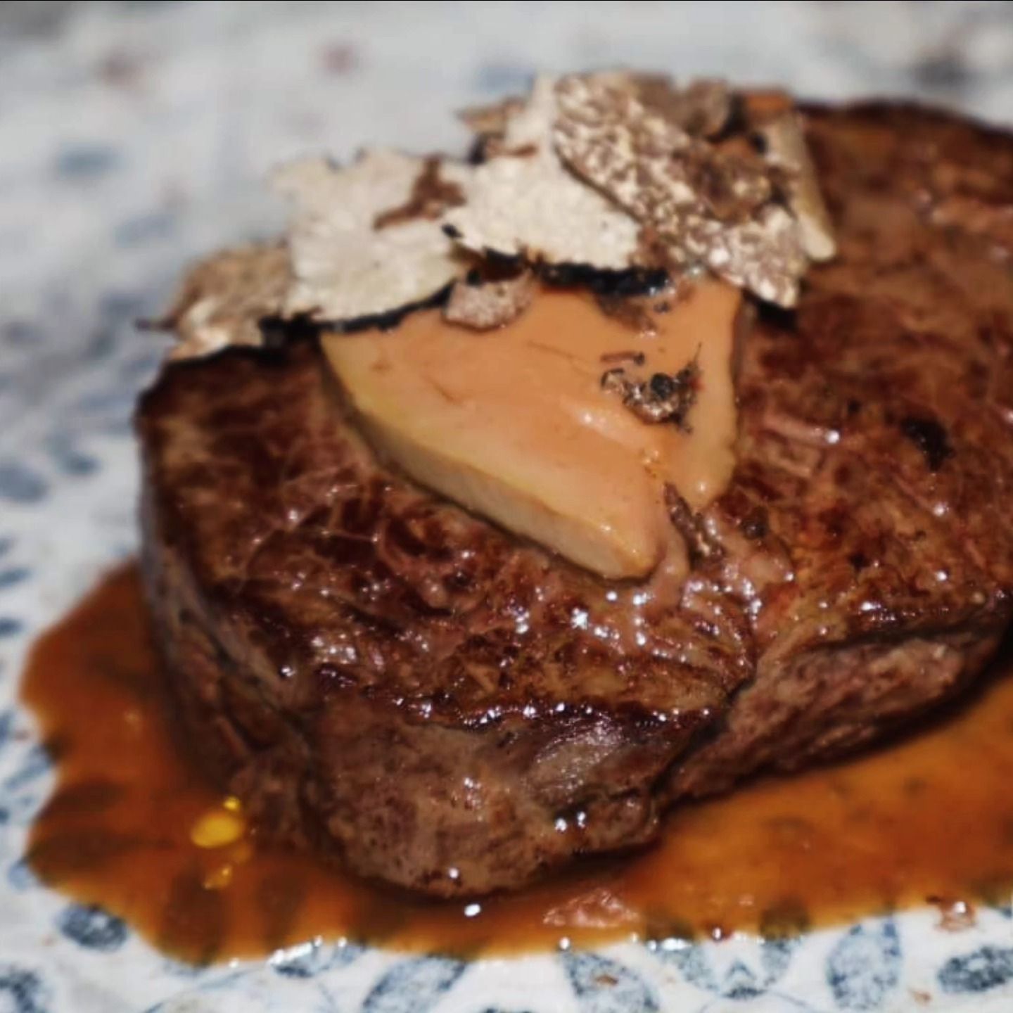 Bistecca scottata con foie gras e tartufo a scaglie, servita con salsa su un piatto bianco.