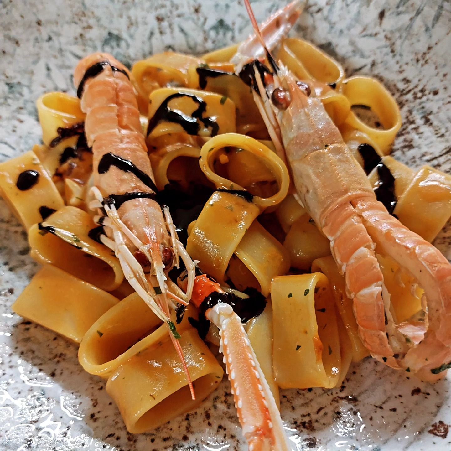 Pappardelle con gamberi, condite con salsa scura e servite su un piatto maculato.