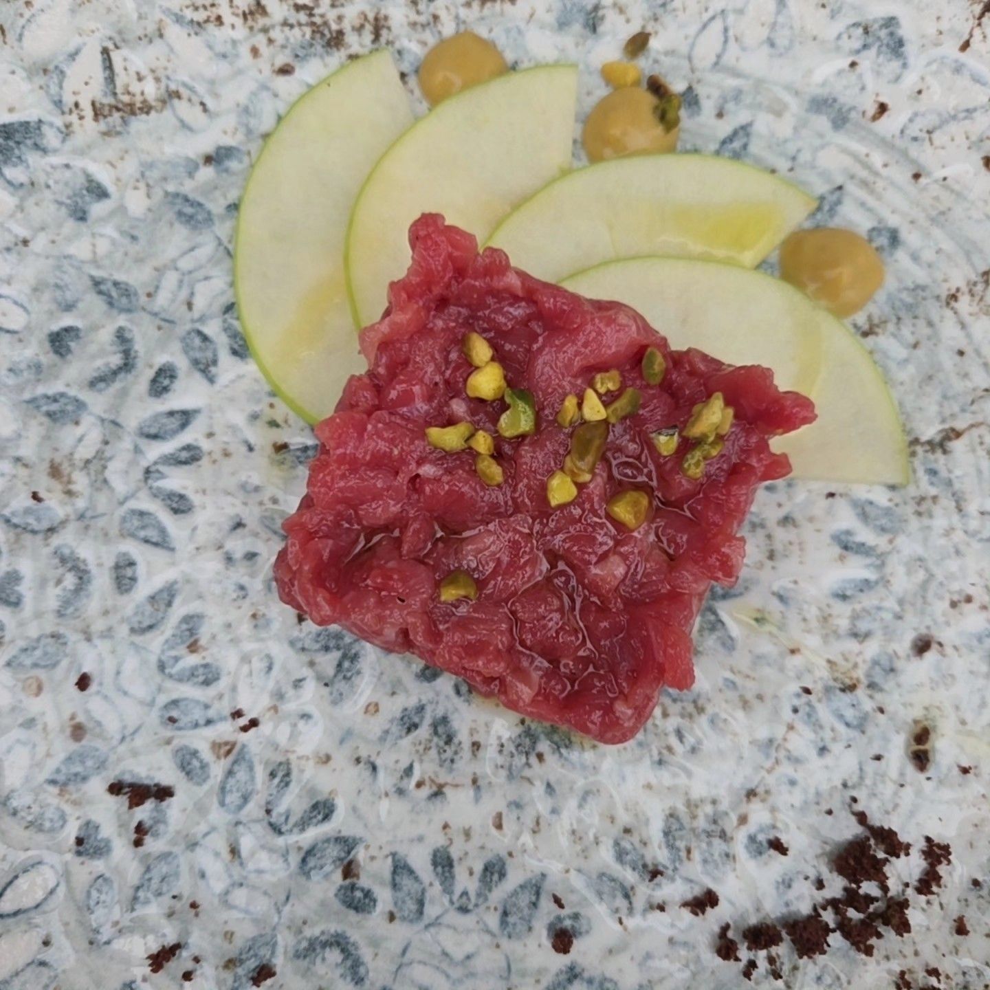 Dessert ai frutti rossi guarnito con pistacchi e fette di frutta verde su un piatto maculato.