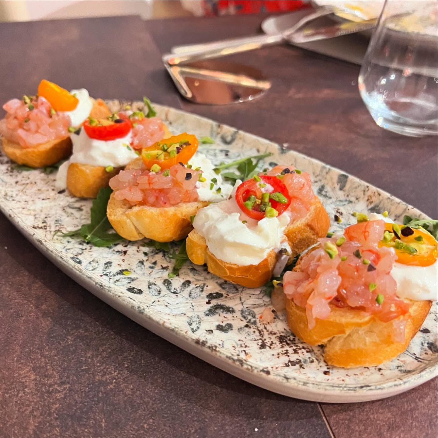 Bruschette servite su un piatto mélange, guarnite con pomodoro, panna ed erbe aromatiche, su un tavolo di ristorante.