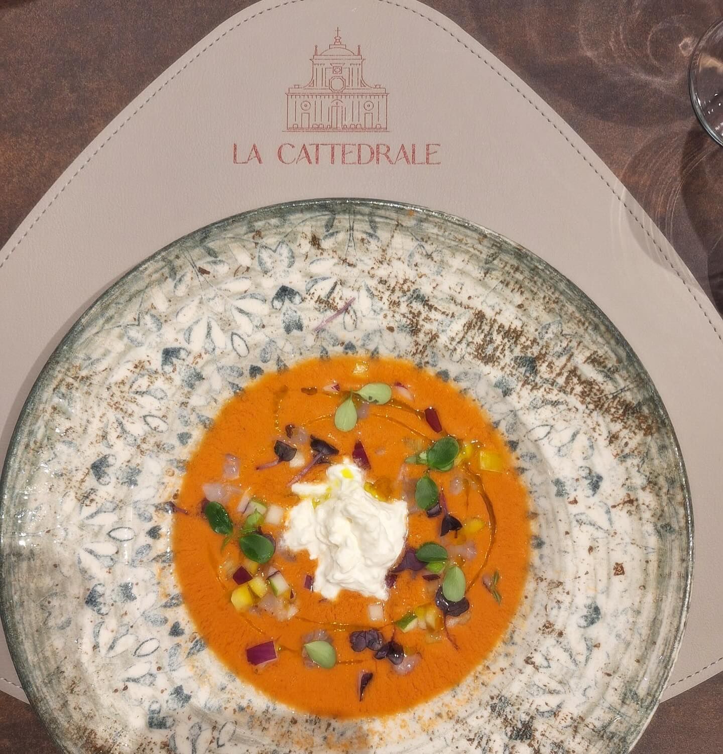 Zuppa cremosa all'arancia in una ciotola maculata, guarnita con erbe aromatiche e panna su una tovaglietta La Cathédrale.