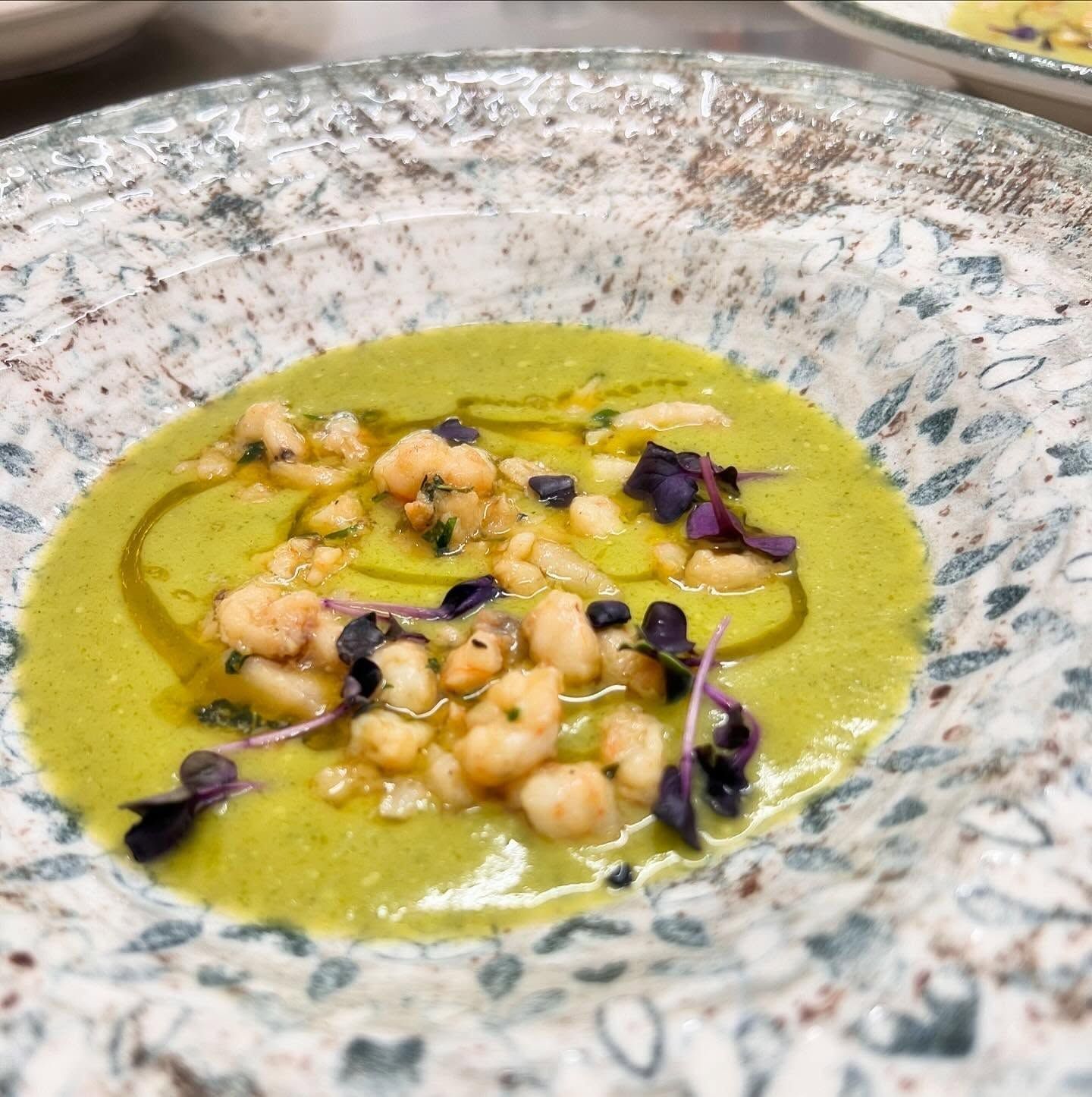 Zuppa verde con gamberetti, microverdure viola e un filo di salsa in una ciotola maculata