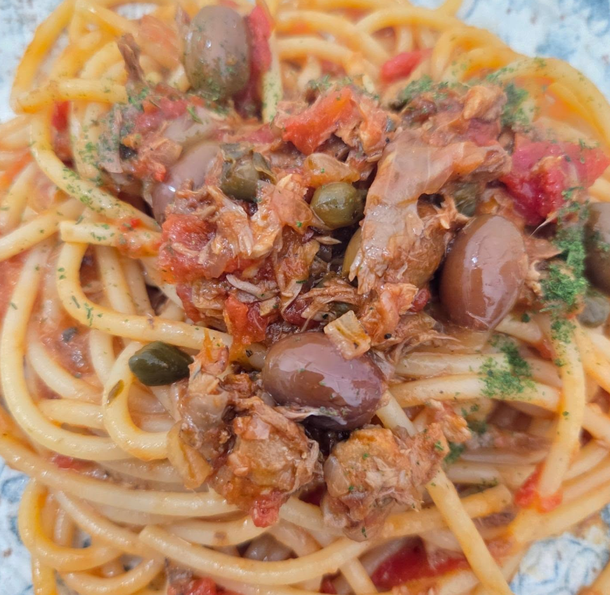 Spaghetti al sugo di pomodoro, tonno e olive verdi su un piatto bianco