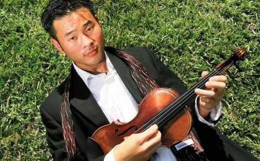 A person in dark scrubs standing in a hospital hallway, hands in their pockets, smiling at the camera.