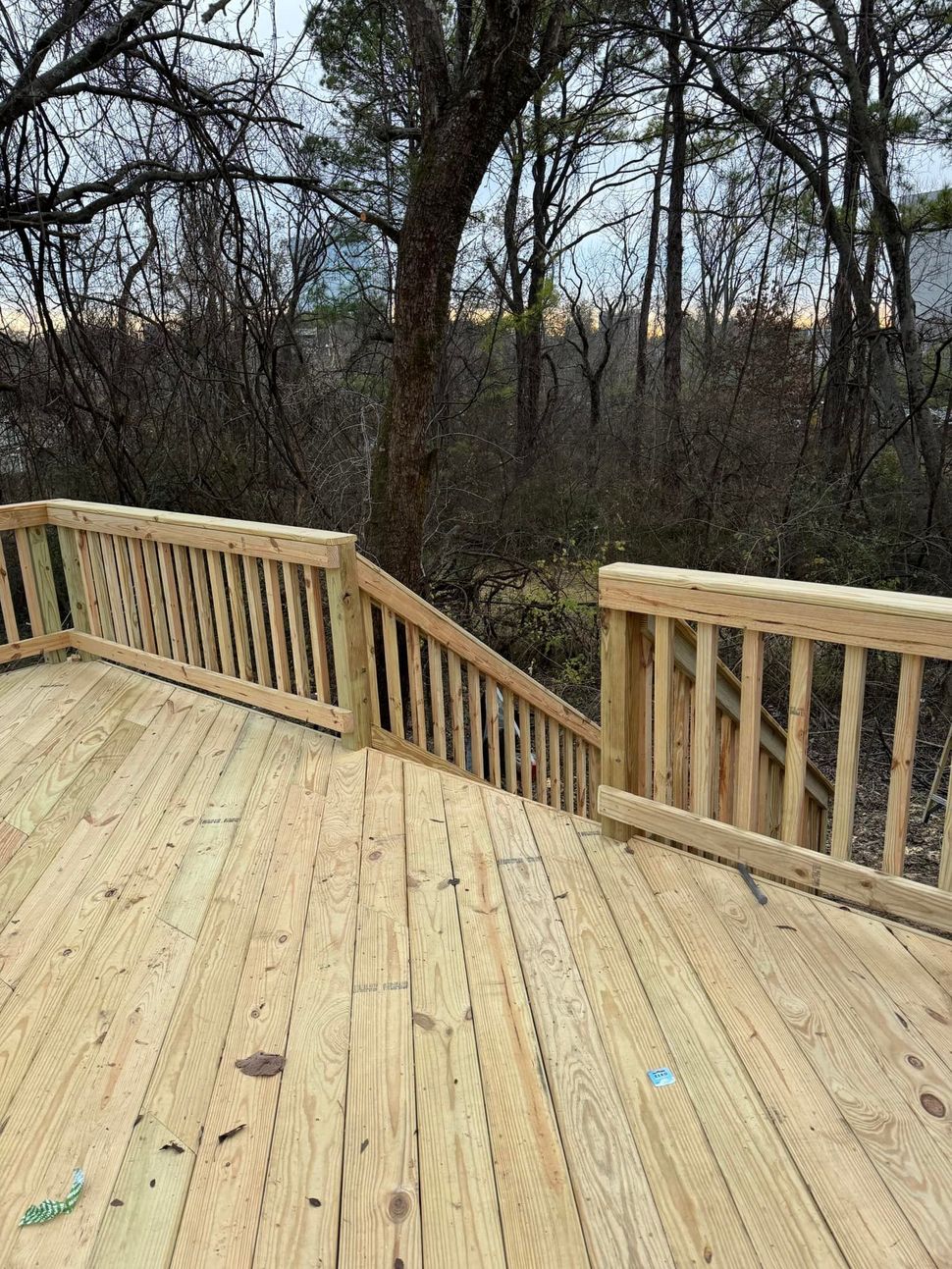 Newly constructed wooden deck with railings, angled steps leading downward, and a background of bare trees.
