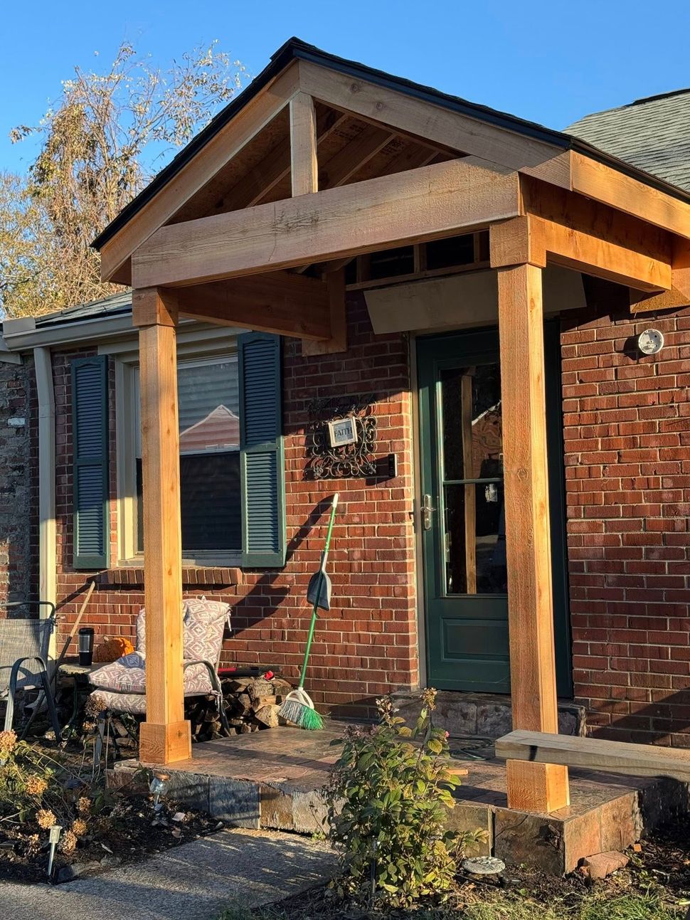 A brick house entrance featuring a newly constructed wooden gabled porch roof supported by two square timber posts.