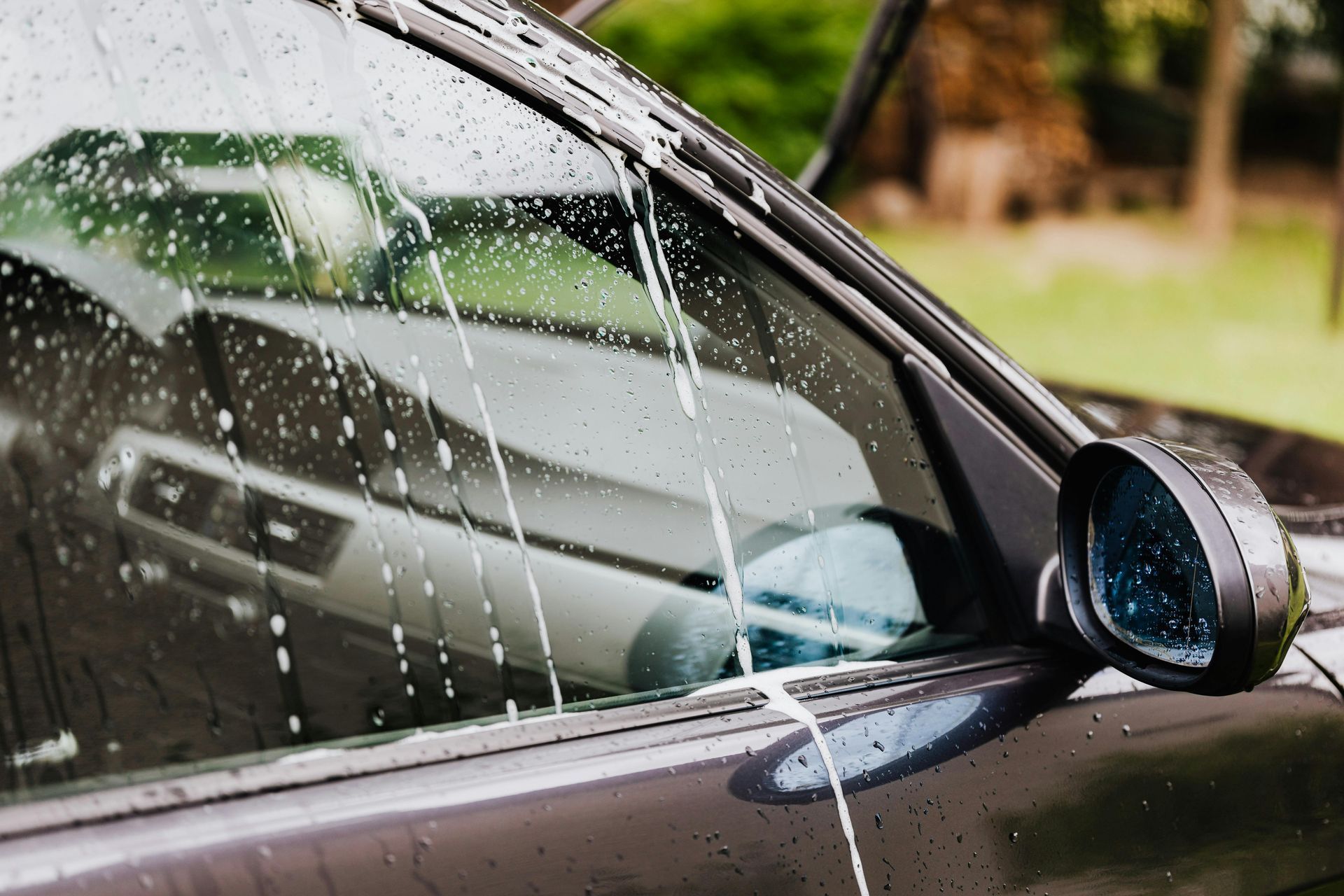 Black car being washed with soapy water; a side mirror and glass window are visible.