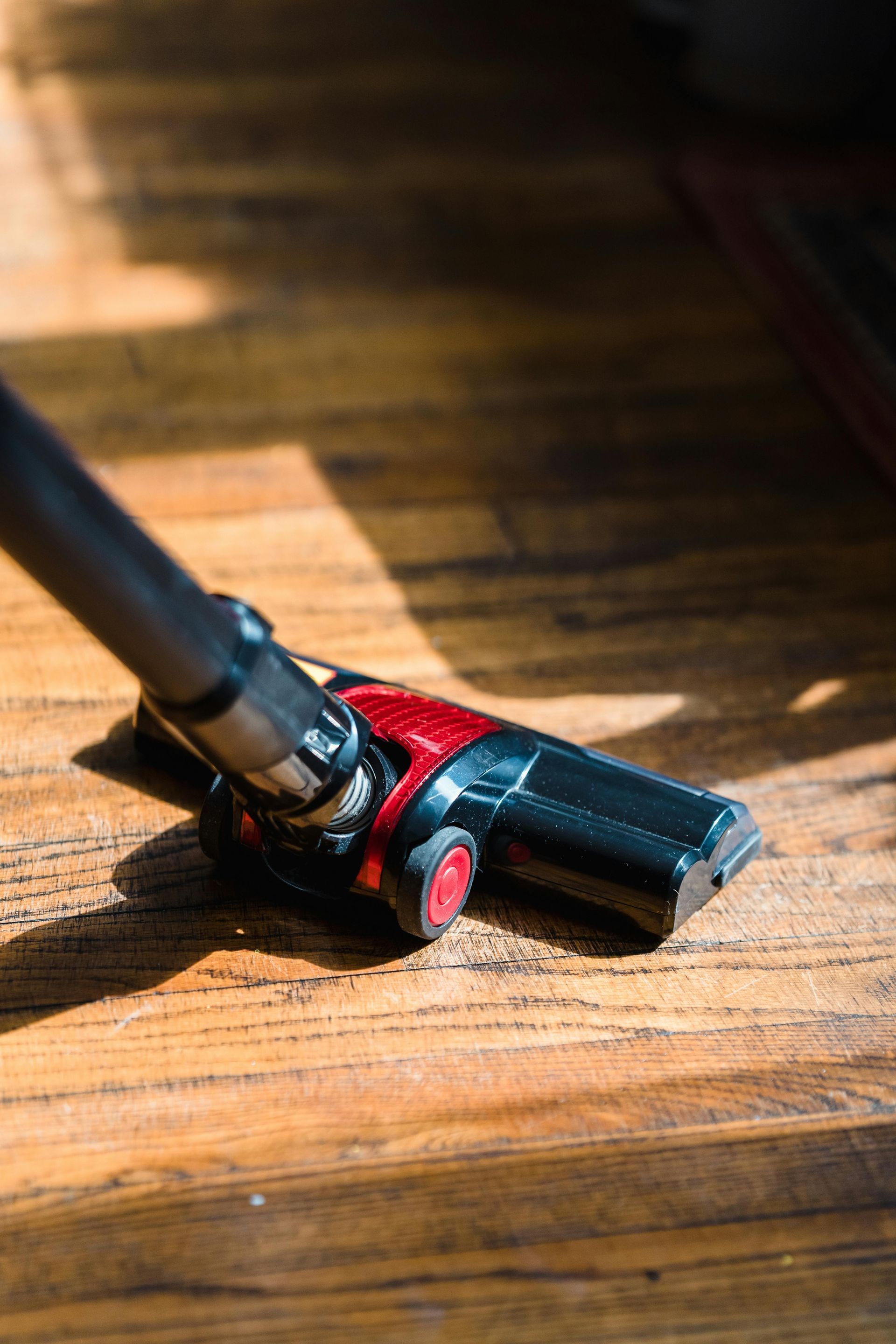 Vacuum head cleaning a wooden floor, partially in sunlight.