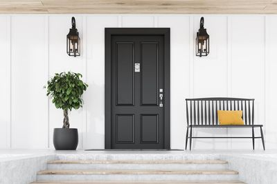 Black front door with lanterns, potted tree, and striped bench on a white porch. Black front door with lanterns, potted tree, and striped bench on a white porch.