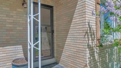 Brick apartment entrance with a glass door, white metal post, and window beside a small potted plant. Brick apartment entrance with a glass door, white metal post, and window beside a small potted plant.