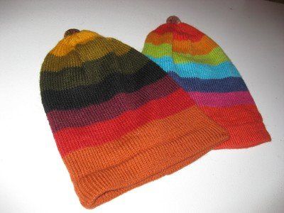 Two colorful knit hats in a rainbow of stripes; one with darker shades and the other with brighter hues.