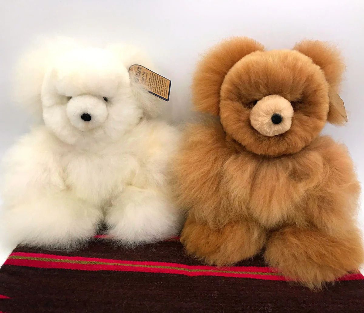 Two fluffy alpaca teddy bears, one white and one brown, sitting on a patterned rug.