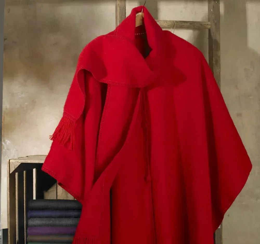 Red cape and scarf hanging on a wooden hanger with a neutral background.