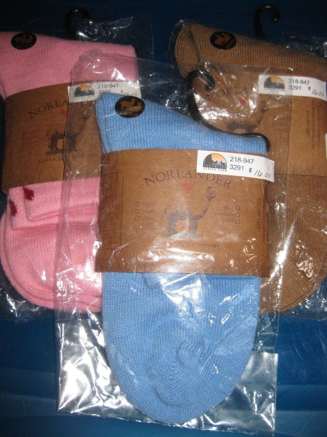 Three pairs of socks, pink, blue, and brown, packaged in clear plastic with brown paper labels.