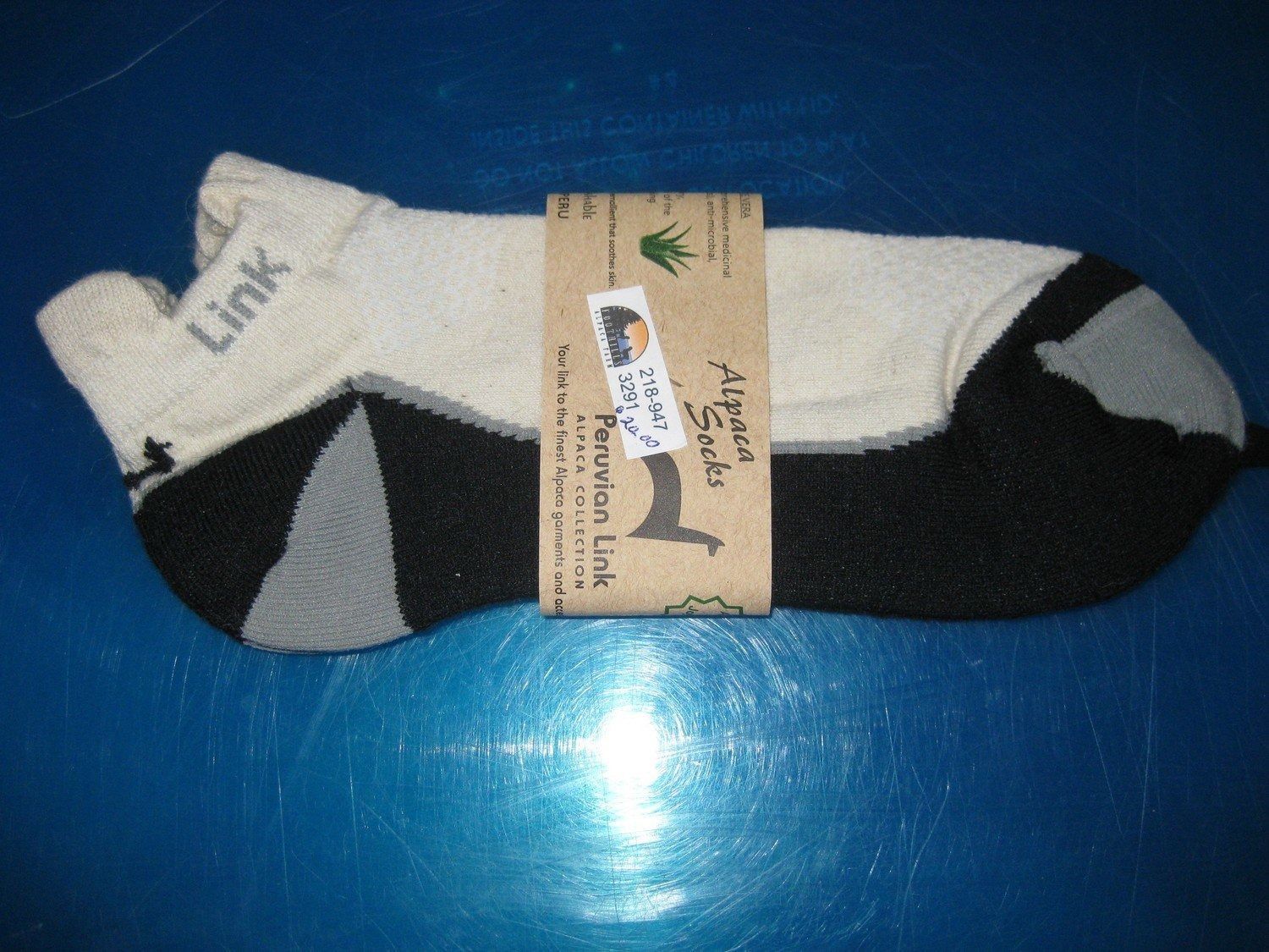 Pair of ankle socks, primarily white, black, and gray, with a cardboard band around them. The band has a drawing and text.