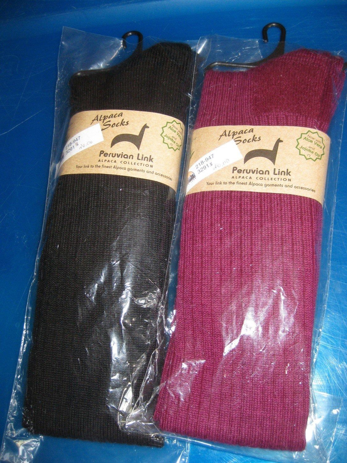 Two pairs of alpaca socks in plastic packaging, one black and one burgundy, each with a brown paper label.