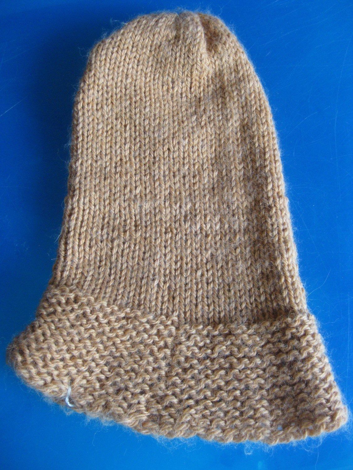 Tan knitted hat with a flared brim on a blue surface.