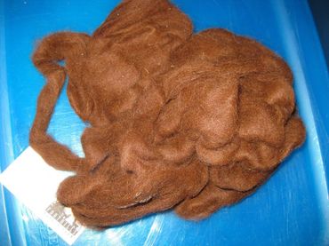 Brown wool fibers clumped together, lying on a blue surface. A white label is partially visible.
