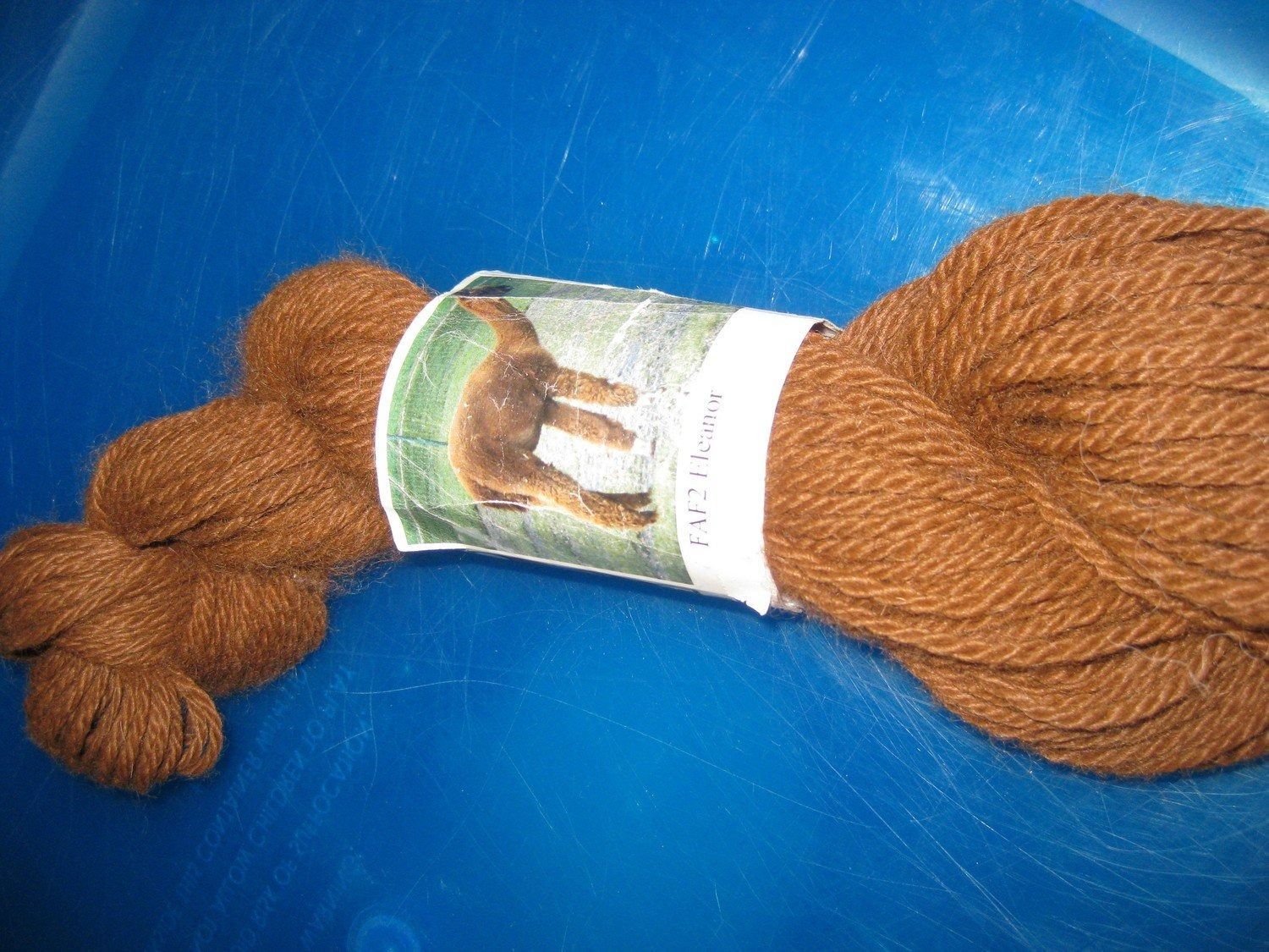Brown yarn skein with a label featuring an alpaca, resting on a blue surface.