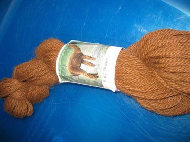 A skein of brown yarn with a label featuring an alpaca, set against a blue background.