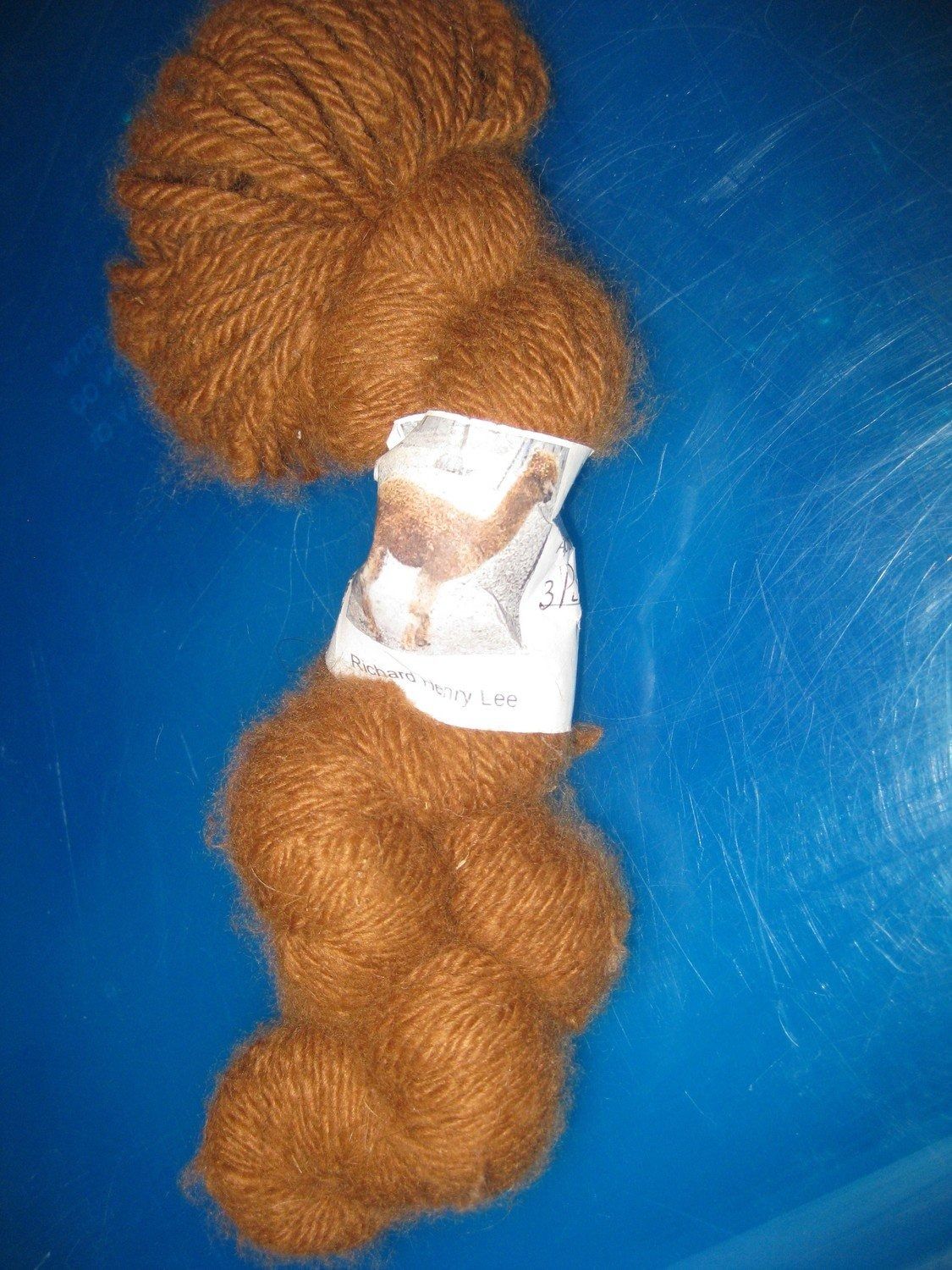 A skein of brown yarn, wrapped with a label, rests on a blue surface.