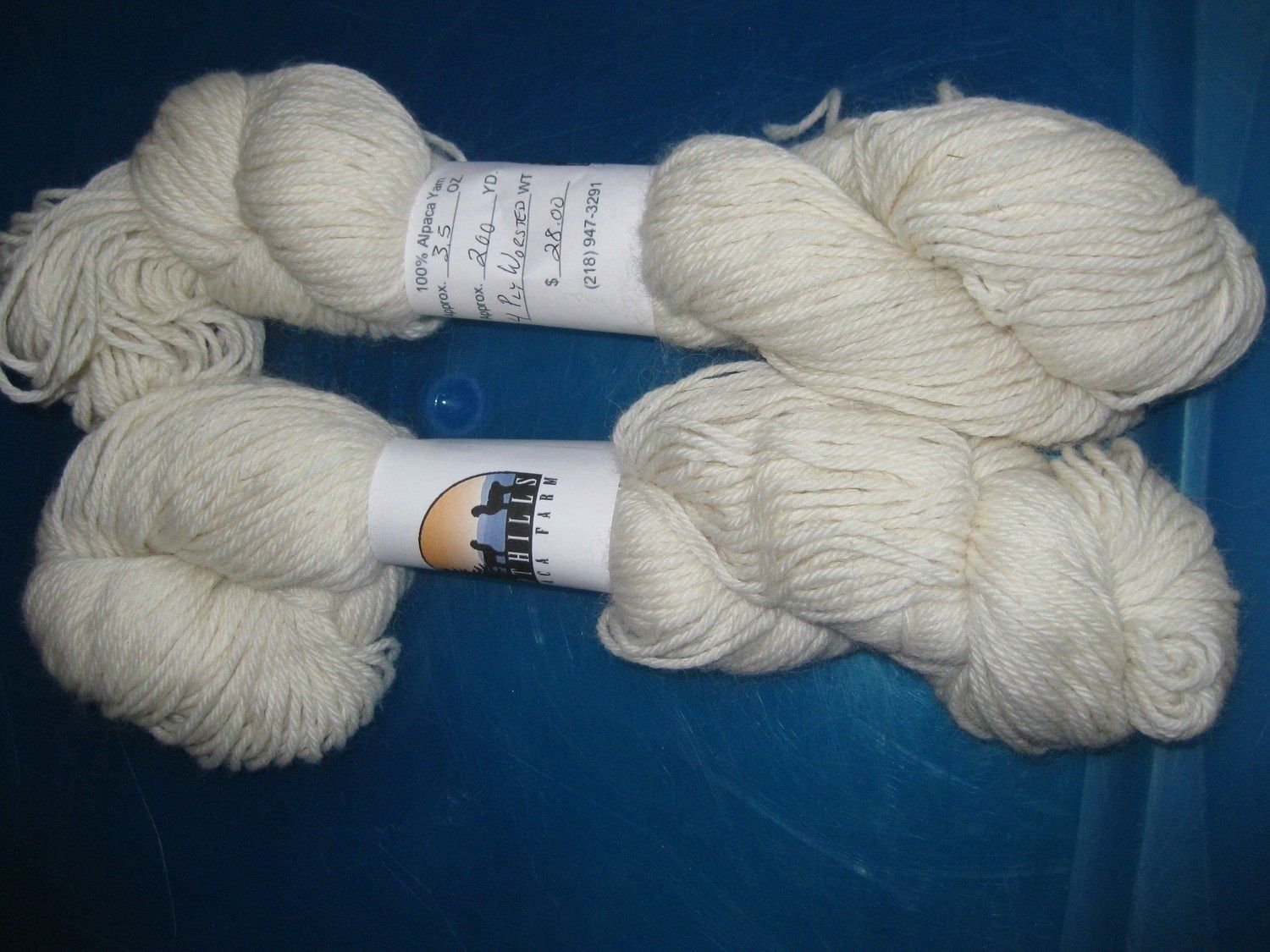 Two skeins of off-white yarn, each with a paper label, resting on a blue surface.