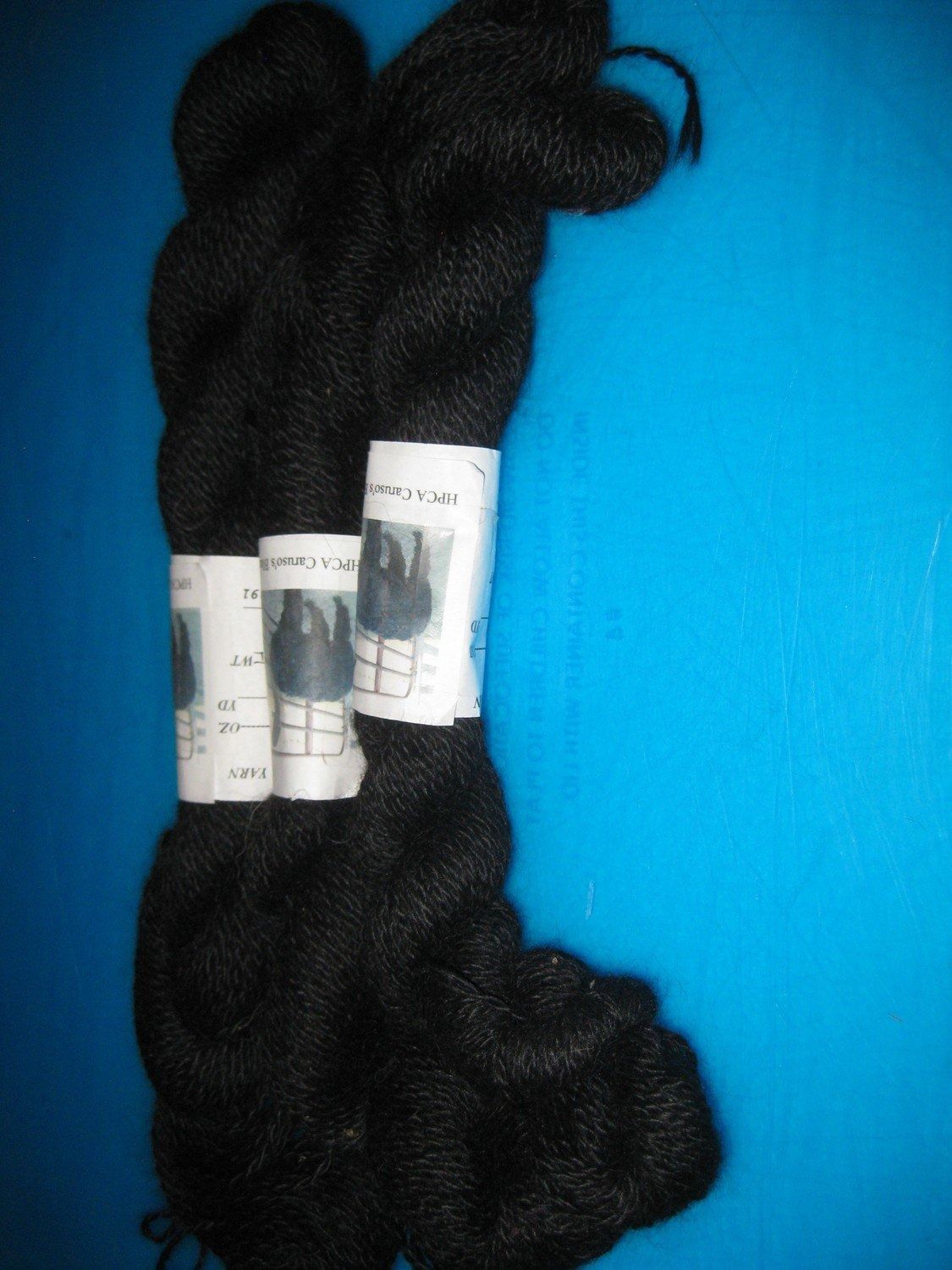 Two skeins of black yarn with white labels, against a blue background.