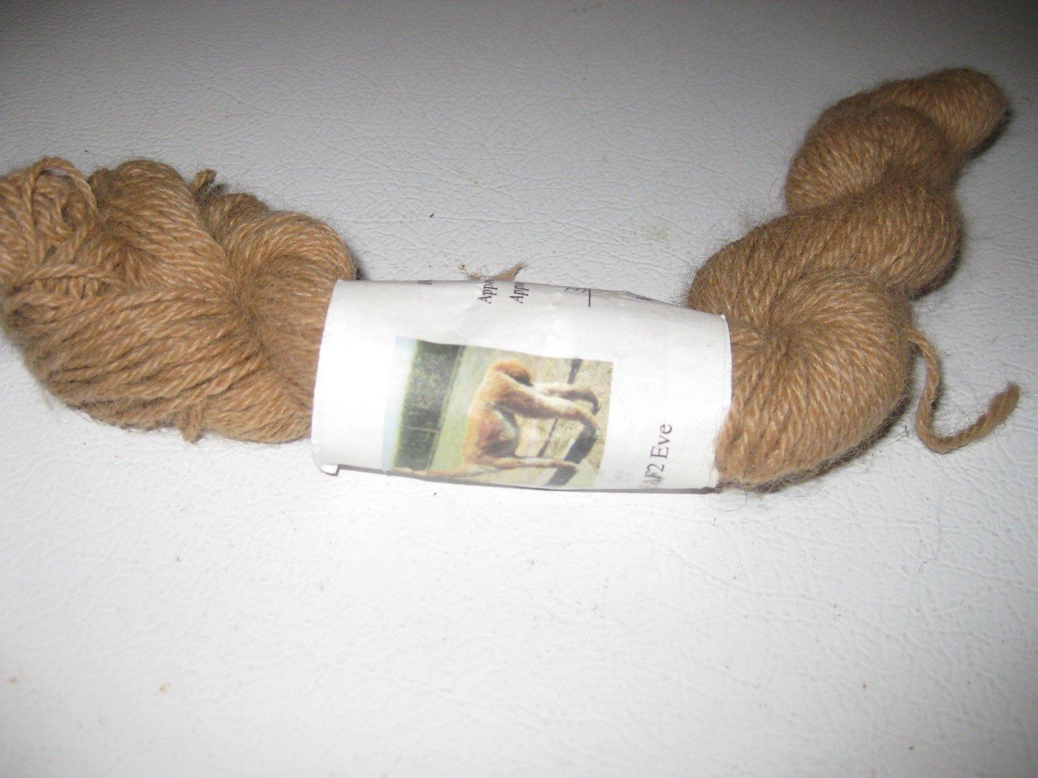 Spool of tan yarn with a white label, likely for knitting or other fiber arts, on a white surface.