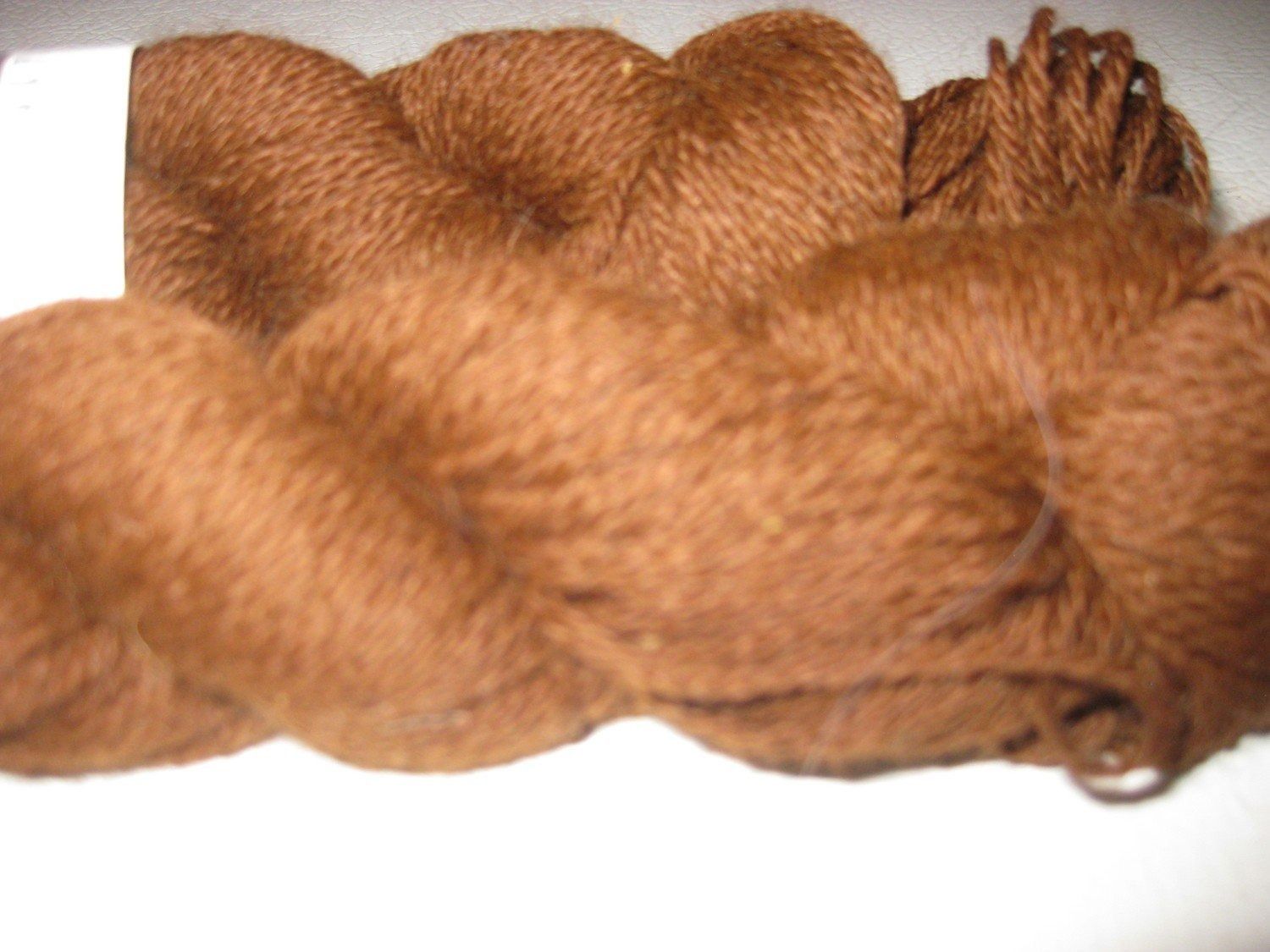 Close-up of three brown skeins of yarn, with soft, textured appearance, on a white surface.
