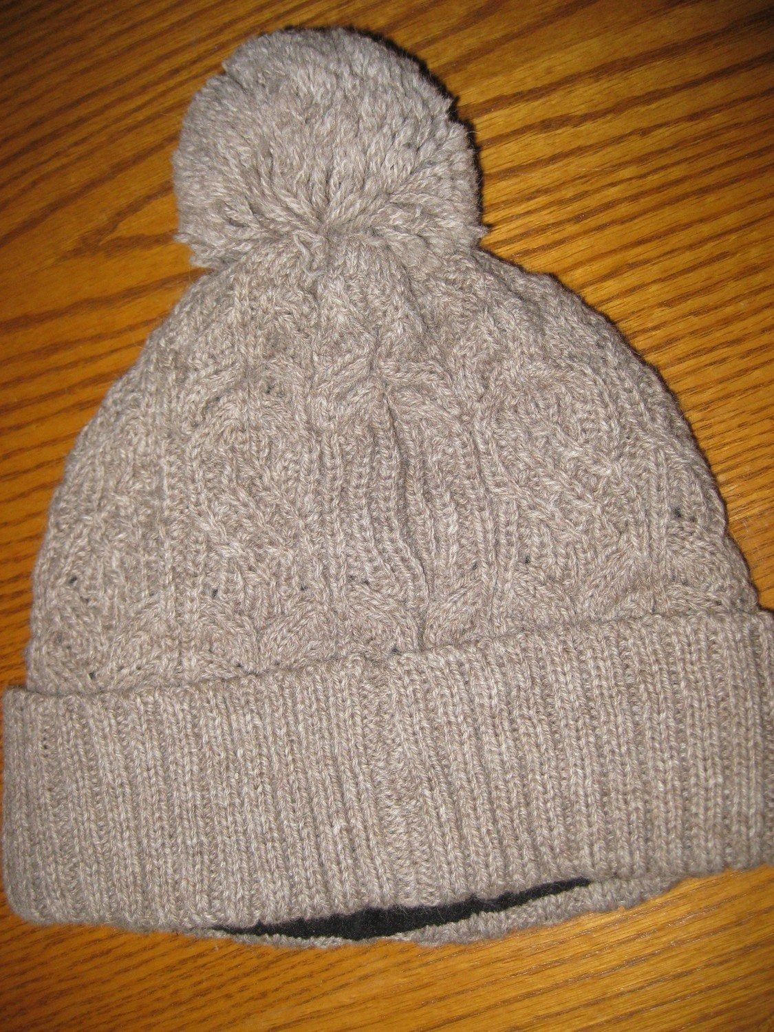 Tan knitted winter hat with a pom-pom, laying on a wooden surface.