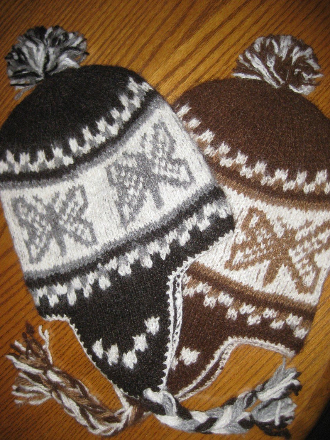 Two knitted earflap hats with butterfly patterns, one black with gray, white, and taupe accents