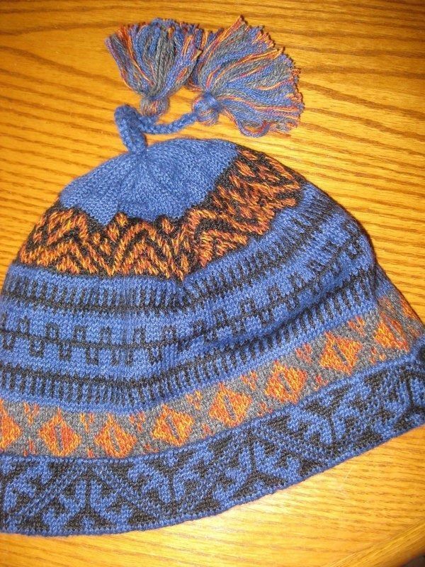 Blue and orange knitted hat with patterned design, a tasseled top, on a wooden surface.