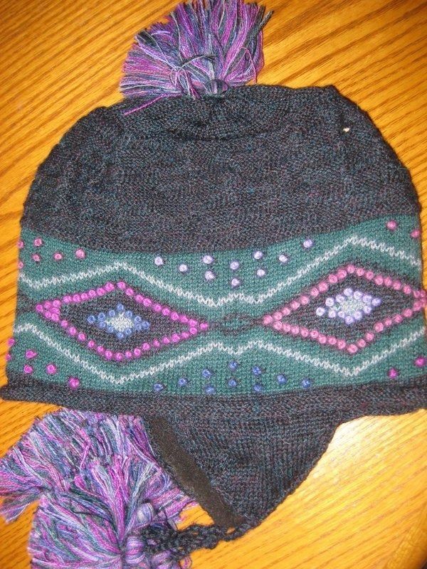Dark blue knit hat with green and pink diamond pattern and purple pom-poms.