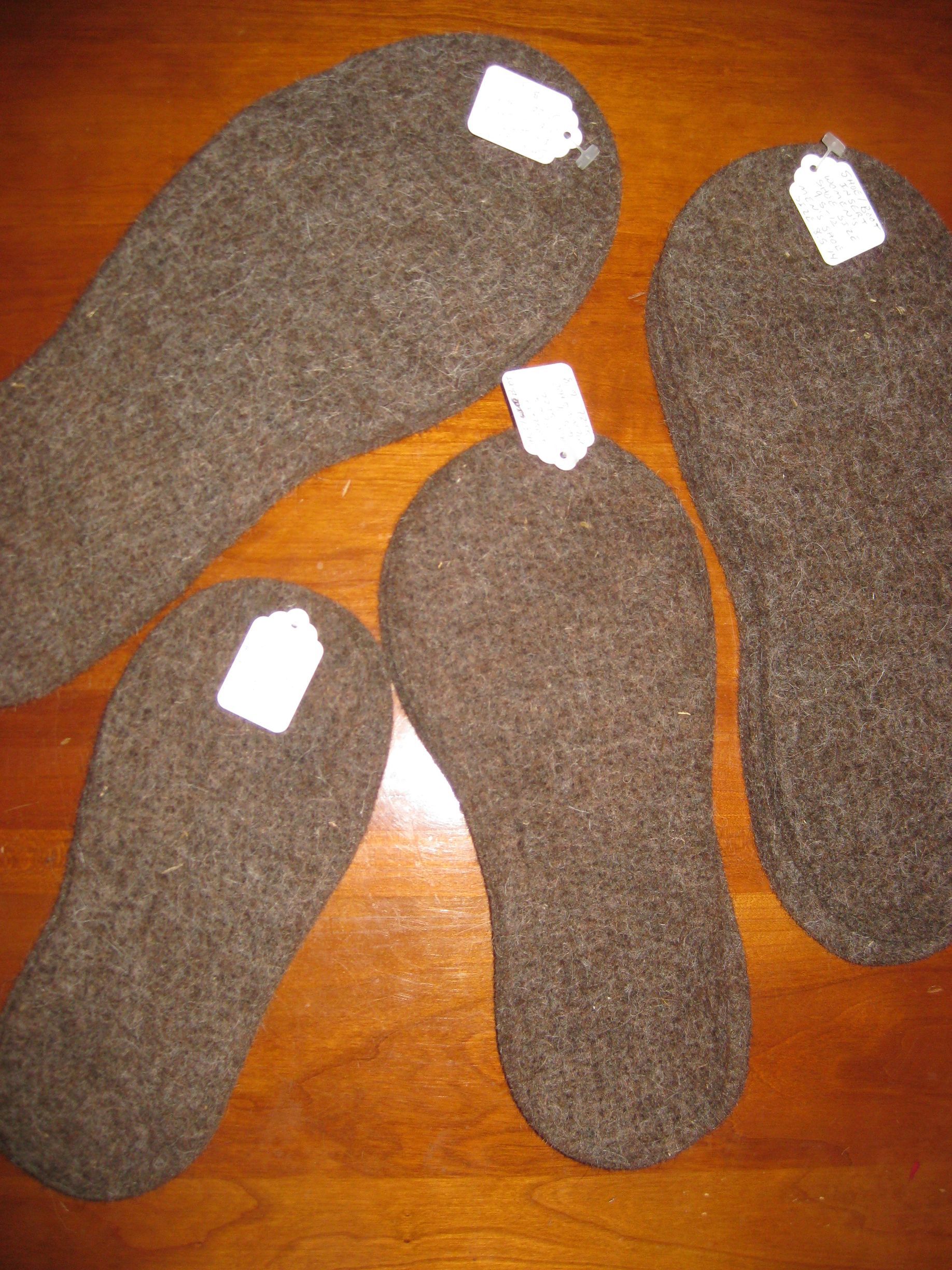 Four brown felt insoles of varying sizes, each with a small white tag, arranged on a wooden surface.