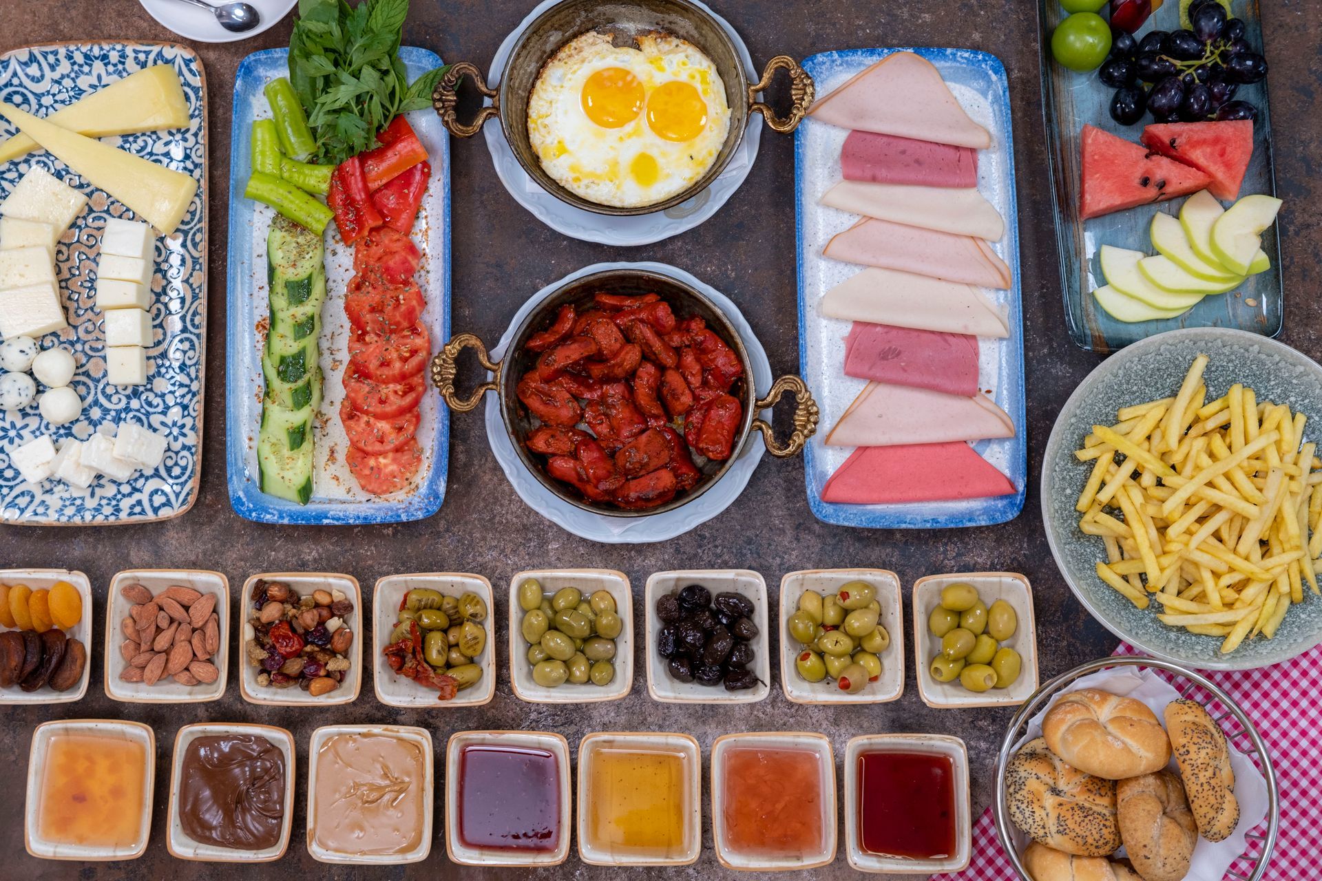 Küçük kaselerde yumurta, pastırma, meyve, hamur işleri, patates kızartması ve çeşitli soslardan oluşan zengin bir açık büfe.