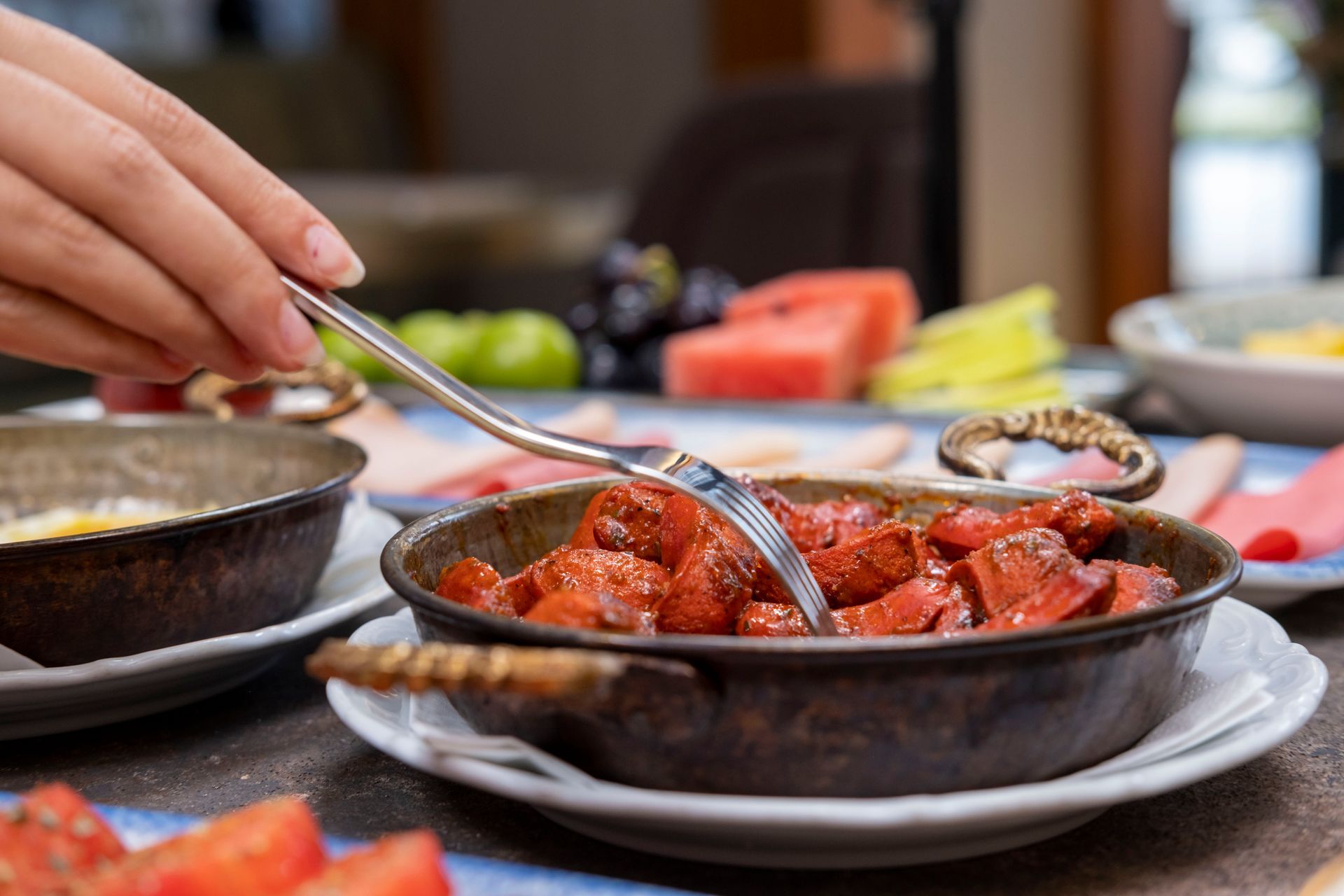 Restoran masasında, arka planda garnitürler bulunan bir kasede, elle kırmızı makarna karıştırılıyor.