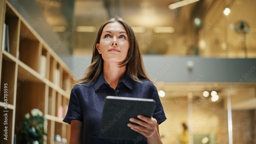 Woman in navy shirt looks up while holding a tablet in an office setting.