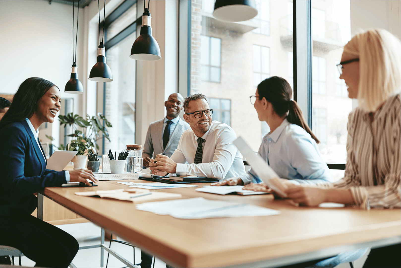 Group of people in business attire at a table, smiling and engaged in discussion; office setting.