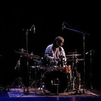 A man is playing drums on a stage in the dark.