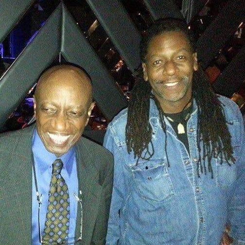 Two men are posing for a picture and one has dreadlocks