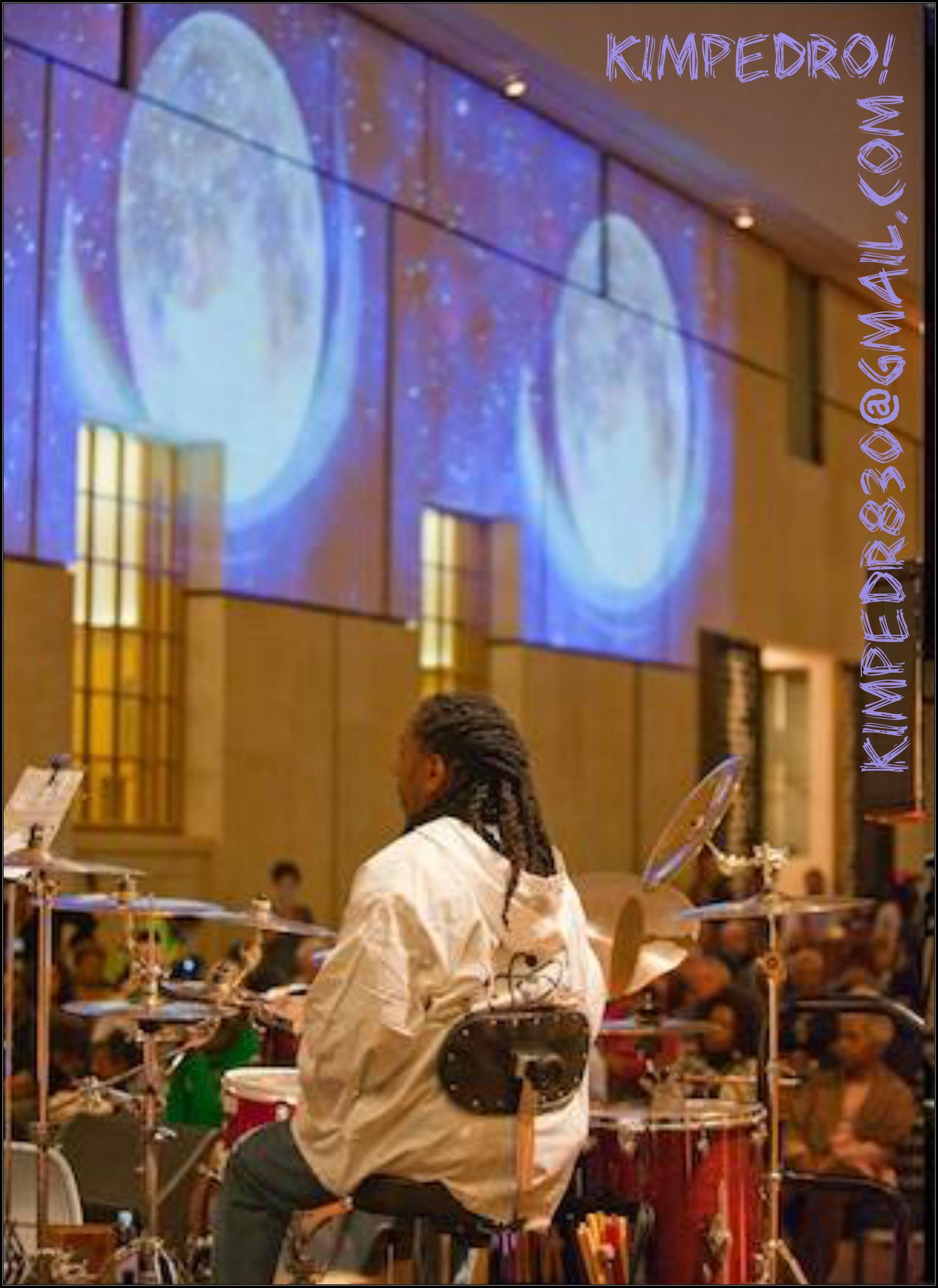 A man playing drums in front of a screen that says kimpedro on it