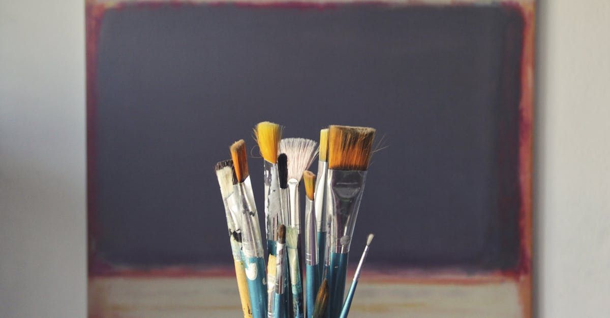 A bunch of paint brushes are sitting on a table in front of a painting.