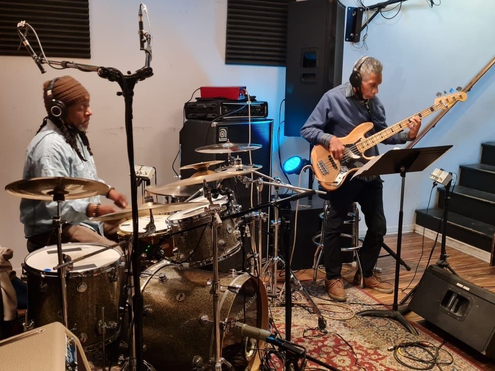 Two men are playing drums and guitars in a room.