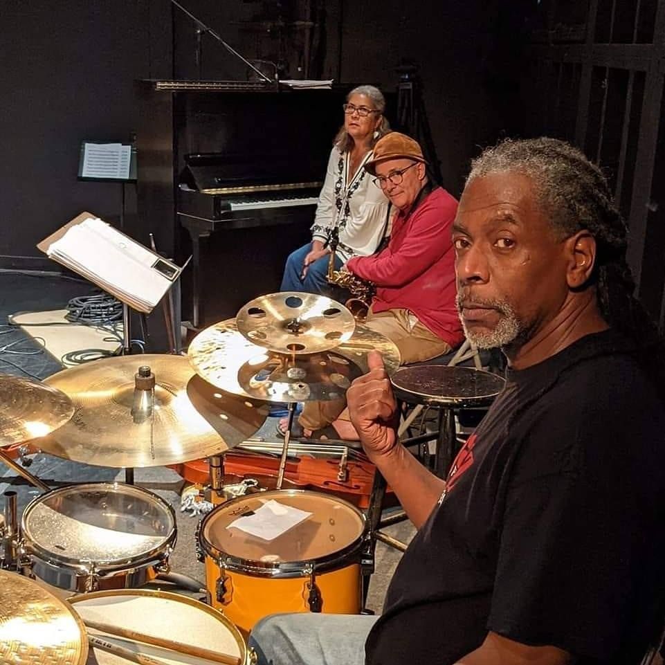 A man sitting in front of a drum set giving a thumbs up