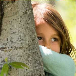 A little girl is peeking out from behind a tree.