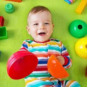 A baby is laying on a green blanket surrounded by toys.
