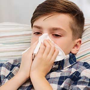 A young boy is blowing his nose with a napkin.